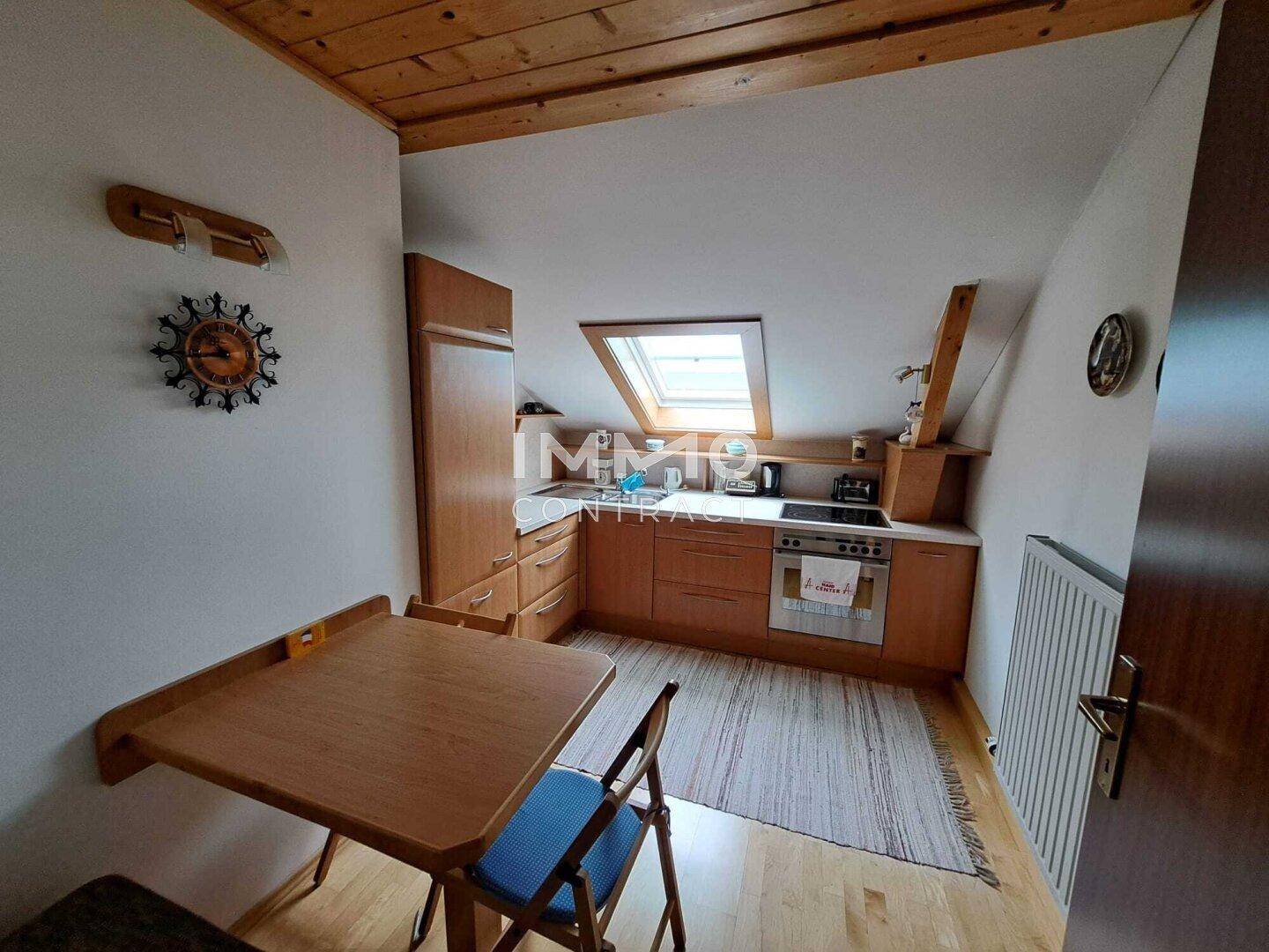 Dachgeschossküche mit Holzeinbauten, Dachfenster und kleinem Esstisch.