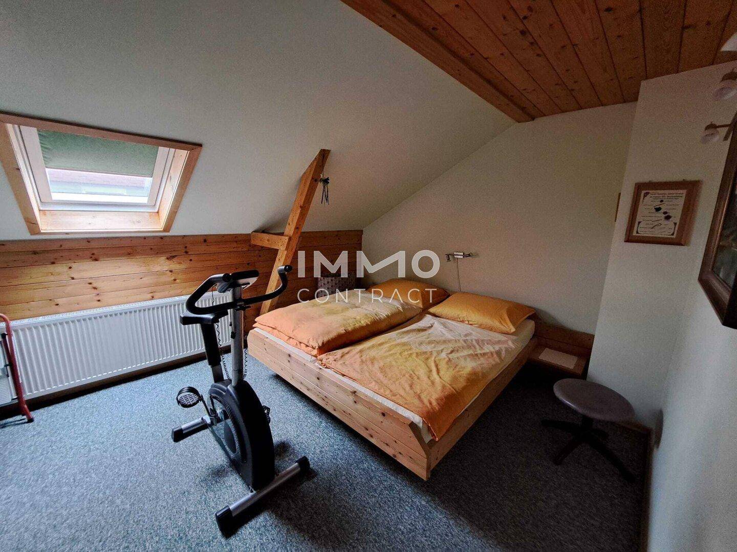 Schlafzimmer im Dachgeschoss mit Holzbett, Heimtrainer und Dachfenster.