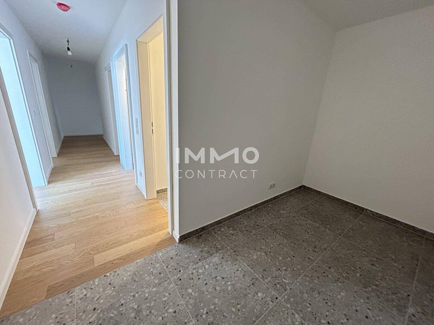 Flur mit Holzboden, der zu einem Zimmer mit Fliesenboden führt, helle Wände.