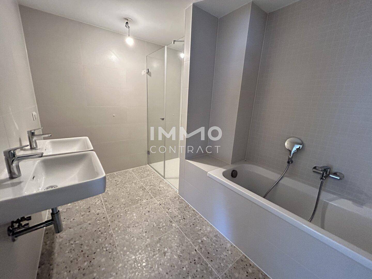 Modernes Badezimmer mit Doppelwaschbecken, Badewanne und Duschkabine, graue Fliesen.