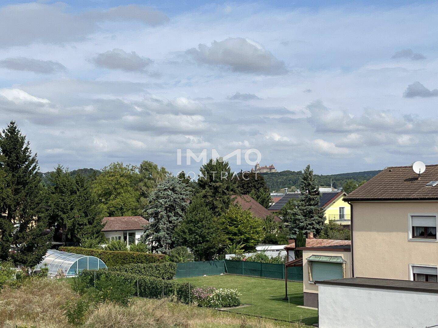 Weitläufiger Ausblick über grüne Gärten und Baumlandschaften mit einem historischen Schloss in der Ferne.