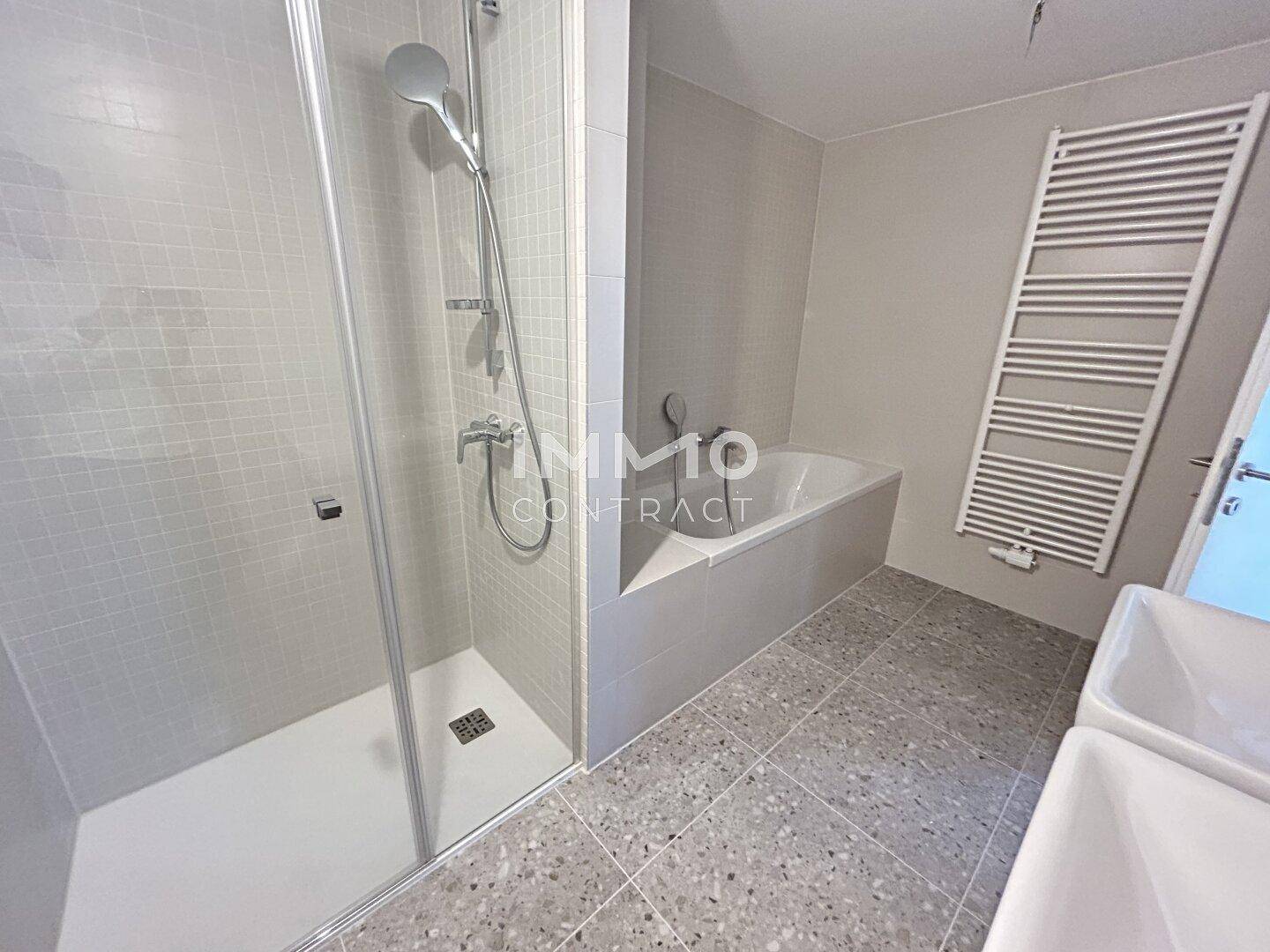 Modernes Badezimmer mit Duschkabine, Badewanne und beheiztem Handtuchhalter, helle Fliesen.