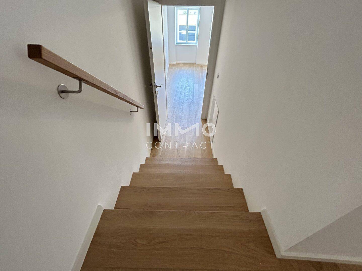 Holztreppe mit Handlauf führt in einen hellen oberen Bereich mit Holzboden.