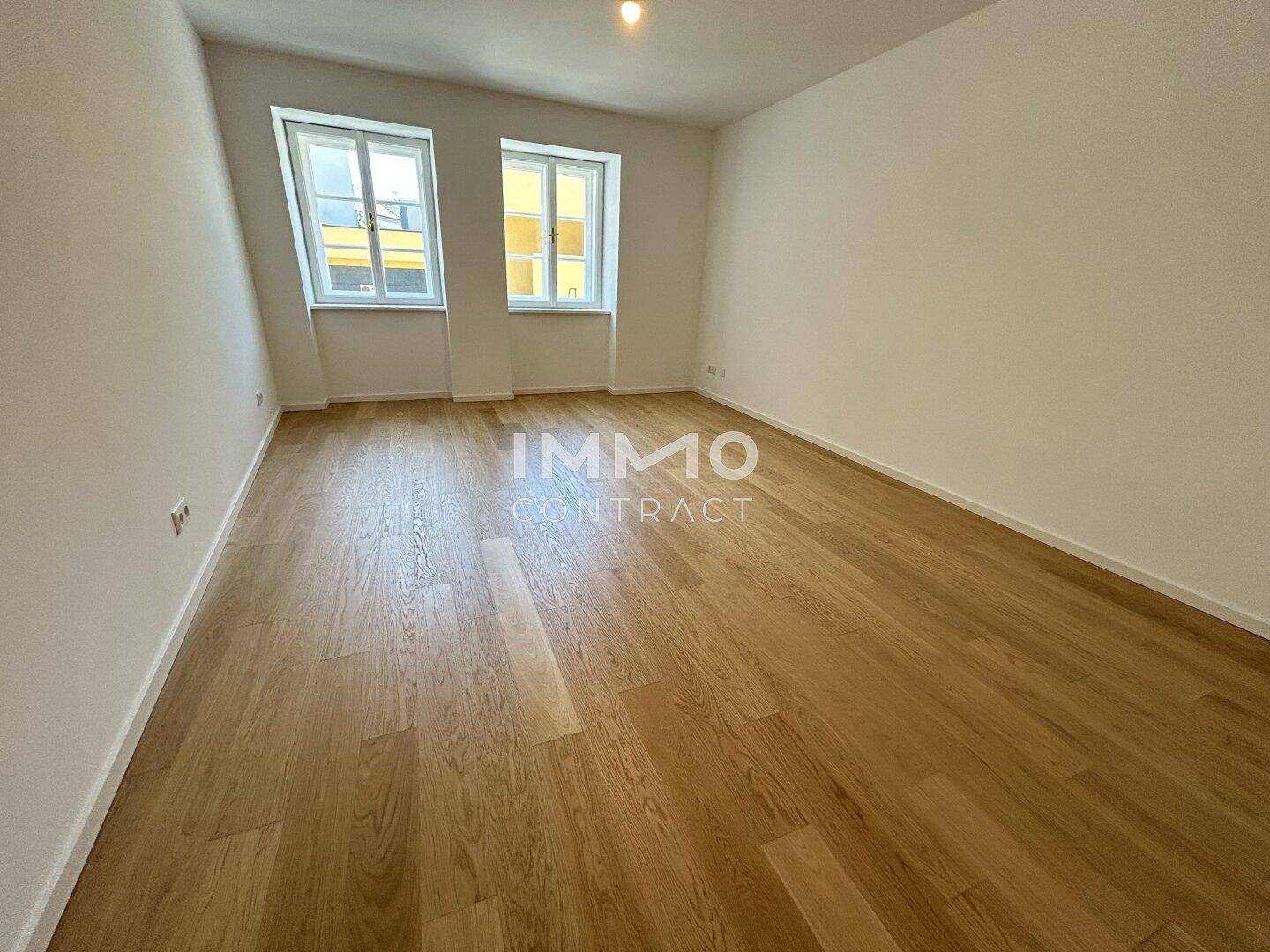 Leeres Zimmer mit Holzboden und zwei Fenstern, bietet viel Tageslicht und flexible Gestaltung.