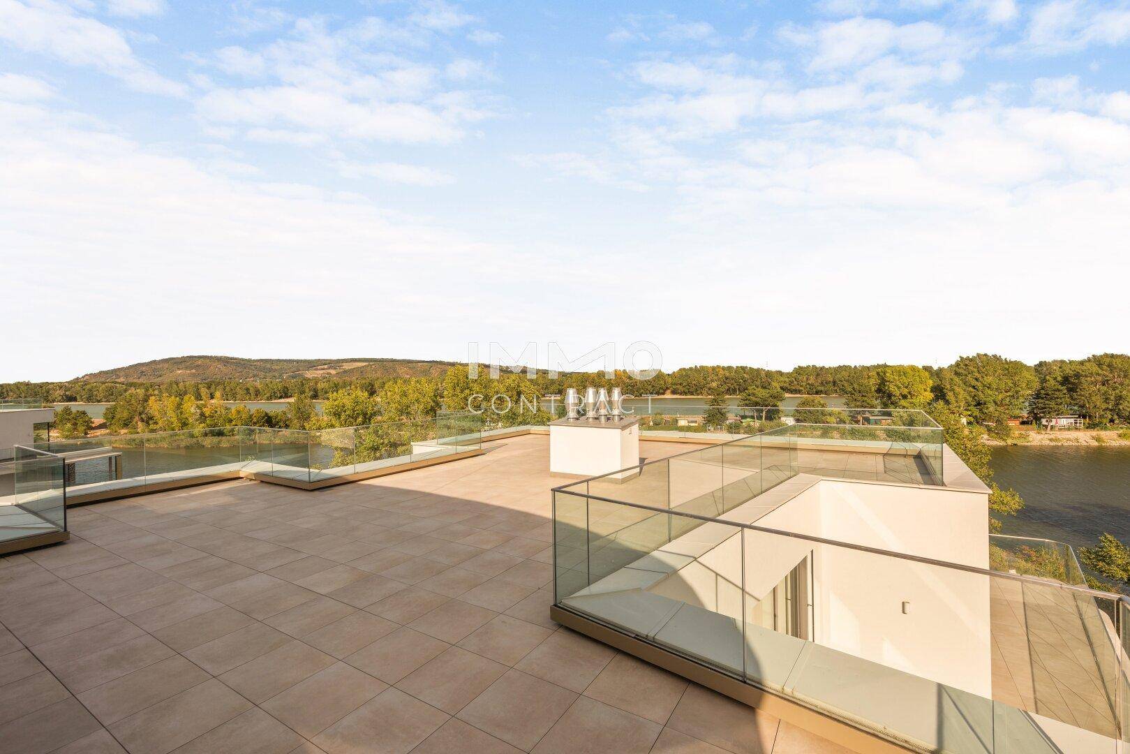 Weitläufige Dachterrasse mit Panoramablick auf den See und die grüne Landschaft unter blauem Himmel.