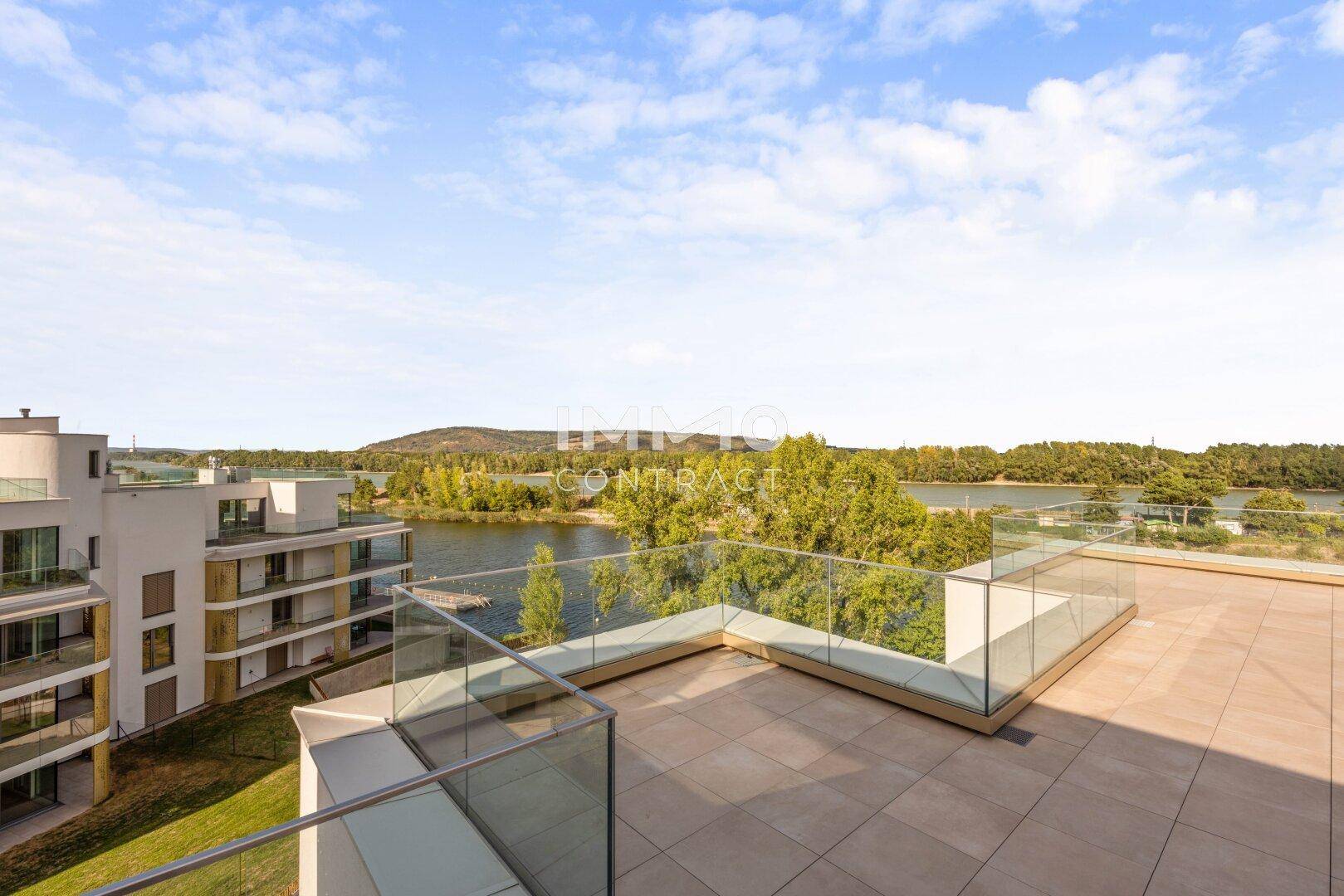Moderne Dachterrasse mit Glasbrüstung und Blick auf die umliegenden Gebäude und den See.