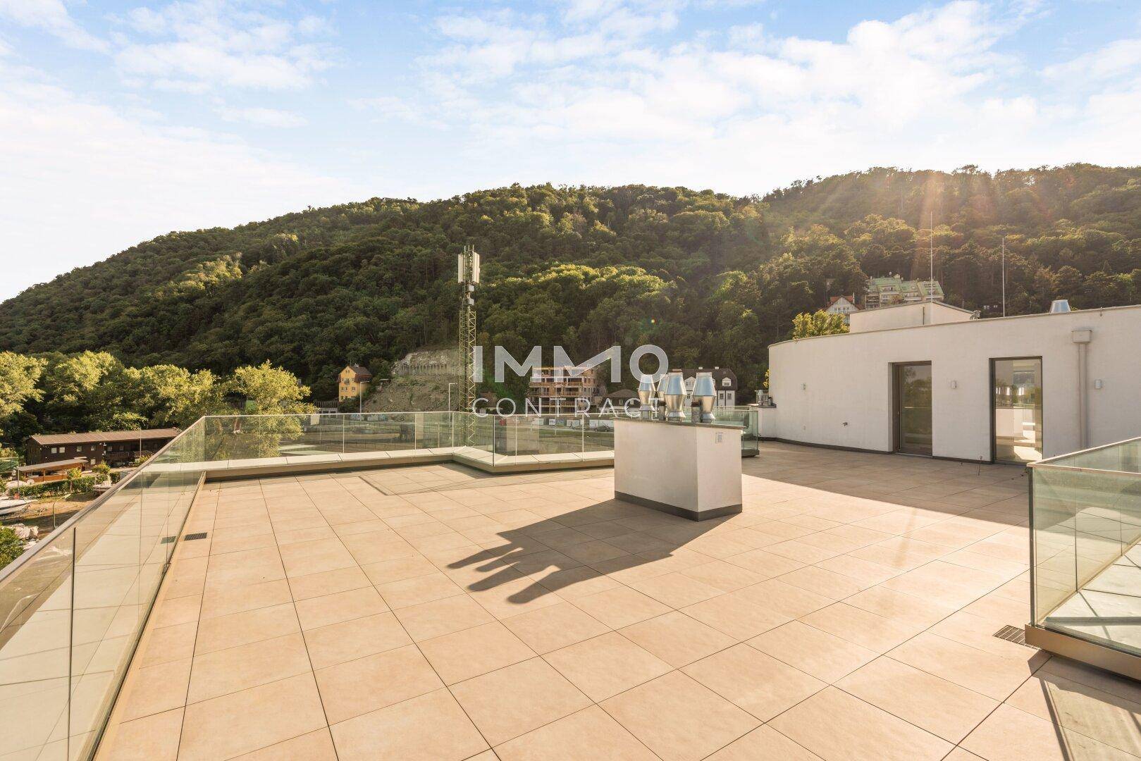Geräumige Dachterrasse mit Blick auf bewaldete Hügel und die umliegende Bebauung unter strahlendem Himmel.