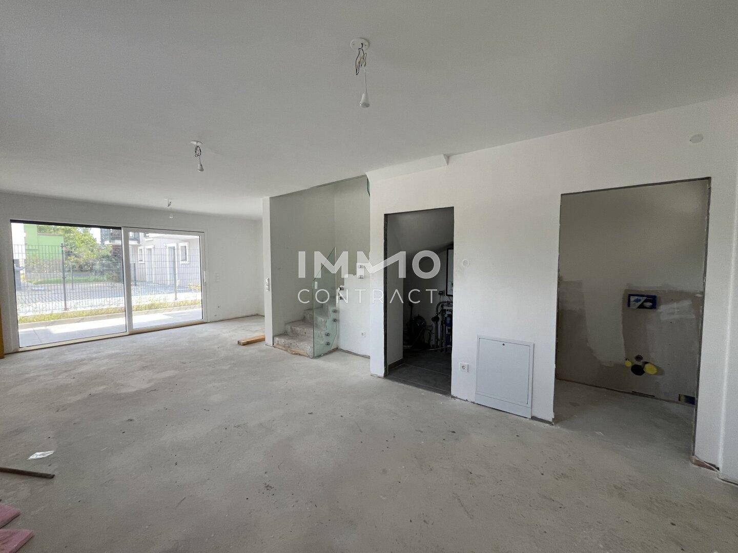 Geräumiger, unfertiger Wohnbereich mit großen Schiebetüren und viel Tageslicht, bereit für den Ausbau.