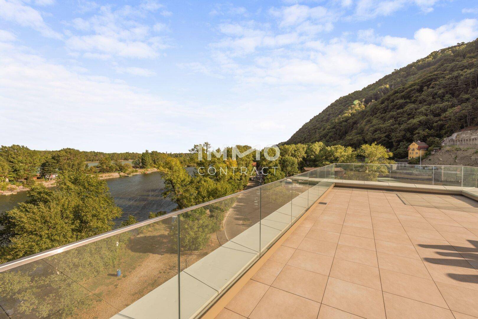 Große Dachterrasse mit Glasgeländer und weitem Blick auf die grüne Landschaft und das Wasser.
