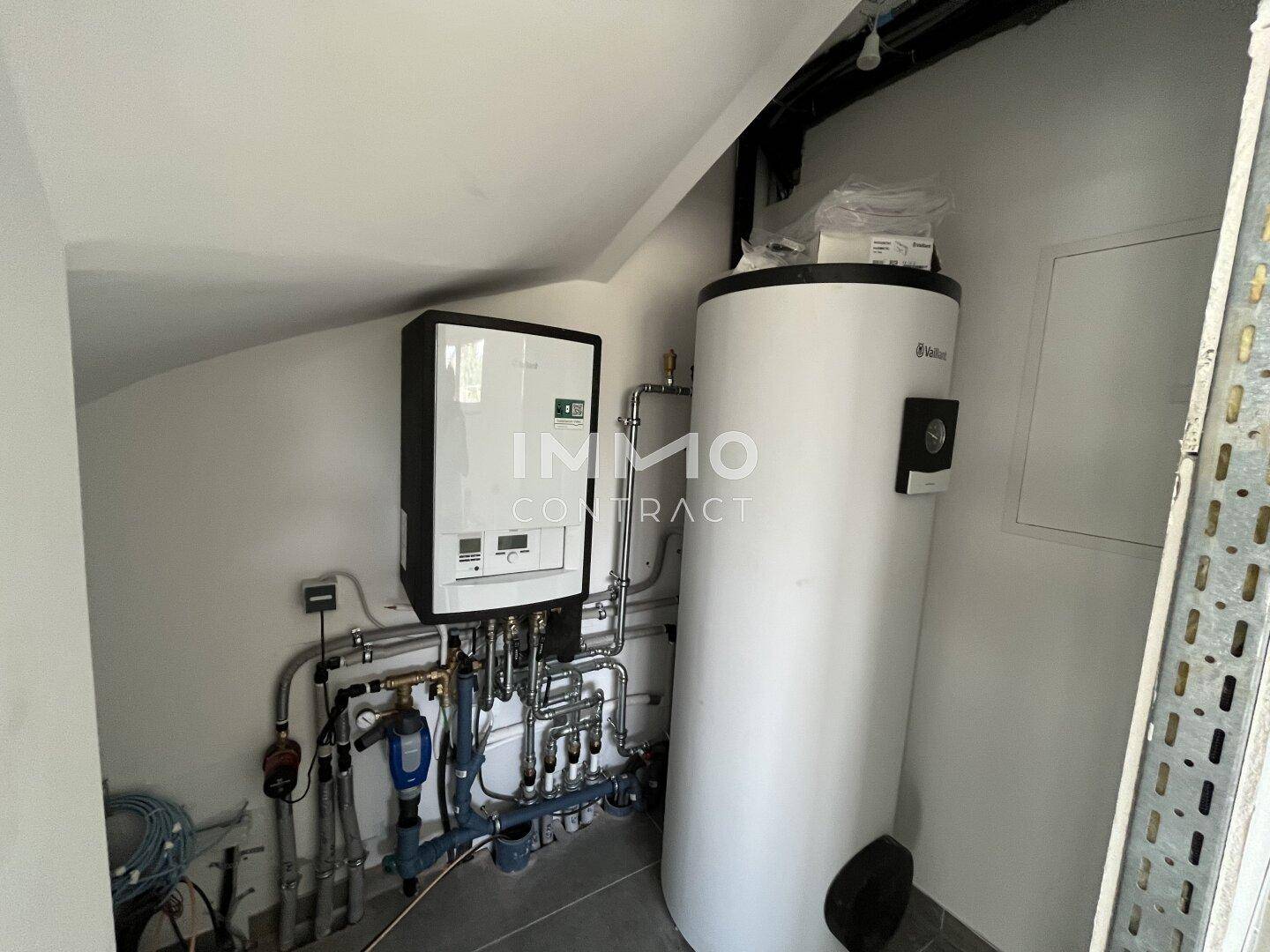 Technikraum mit moderner Heizungsanlage und Warmwasserspeicher in einem neu errichteten Gebäude.