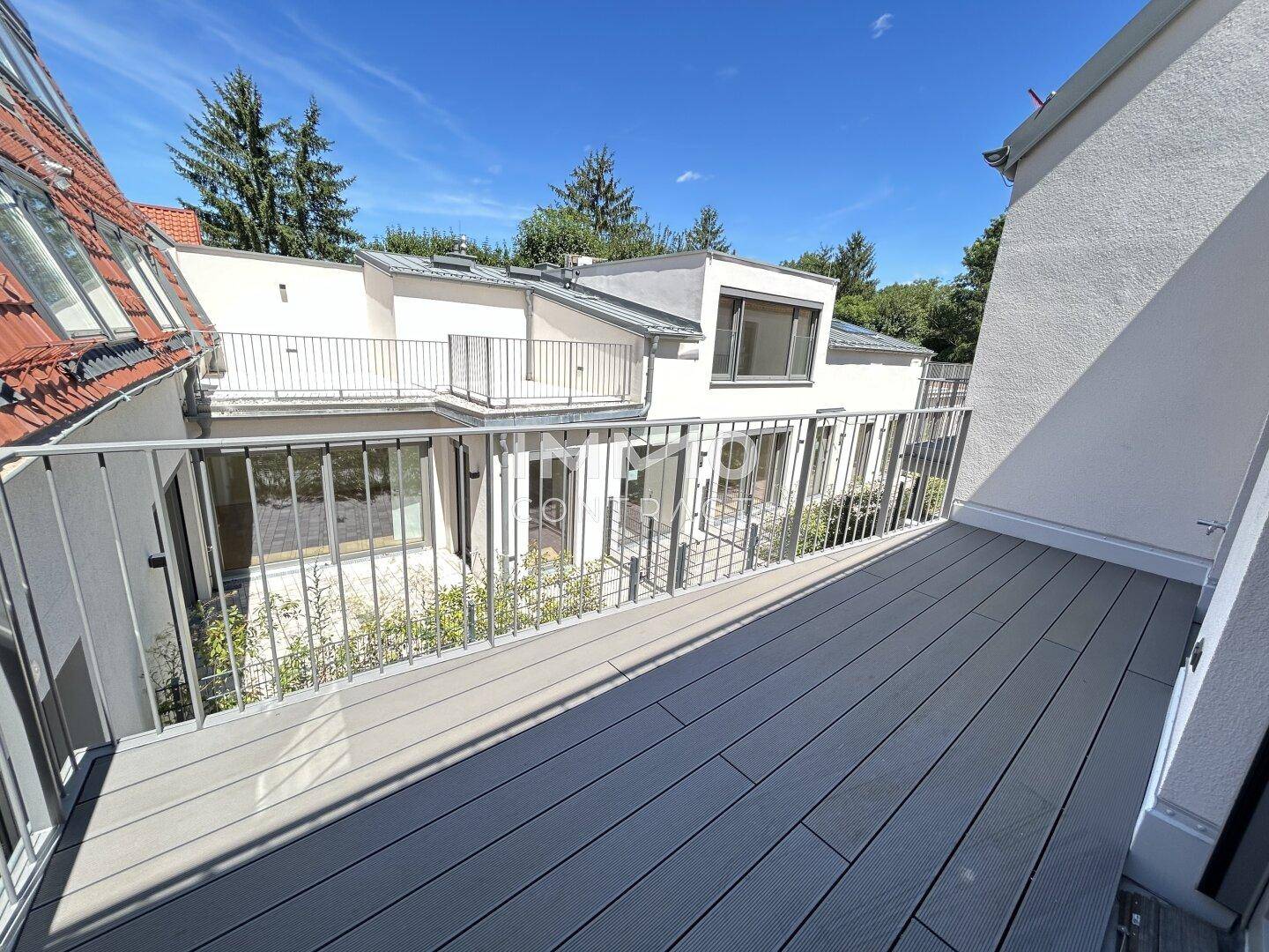Langer Balkon mit Metallgeländer und Blick auf die Nachbargebäude und Grünflächen.