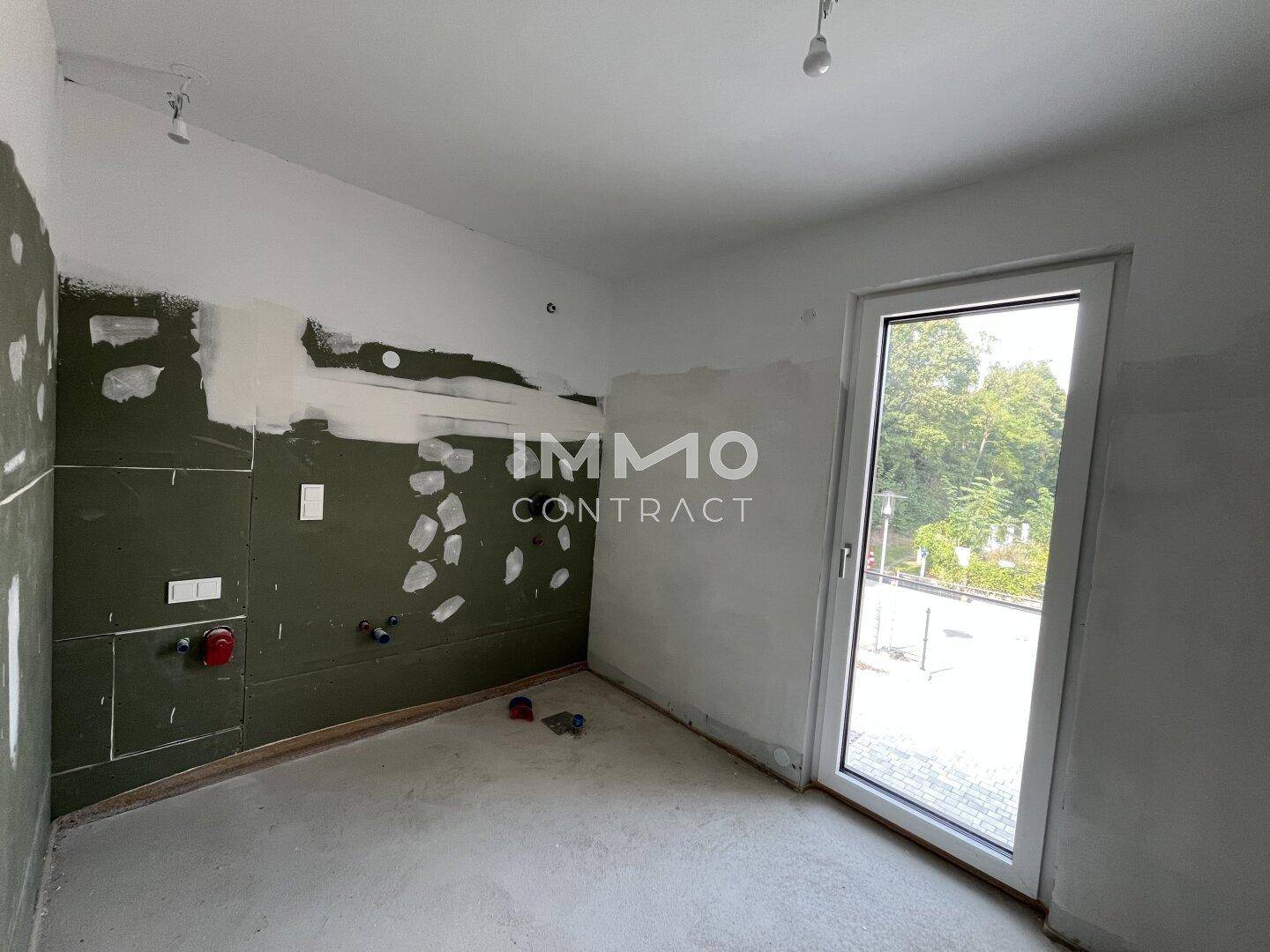 Unfertige Küche mit vorbereiteten Anschlüssen und einem Fenster mit Blick ins Grüne, bereit für die Installation.