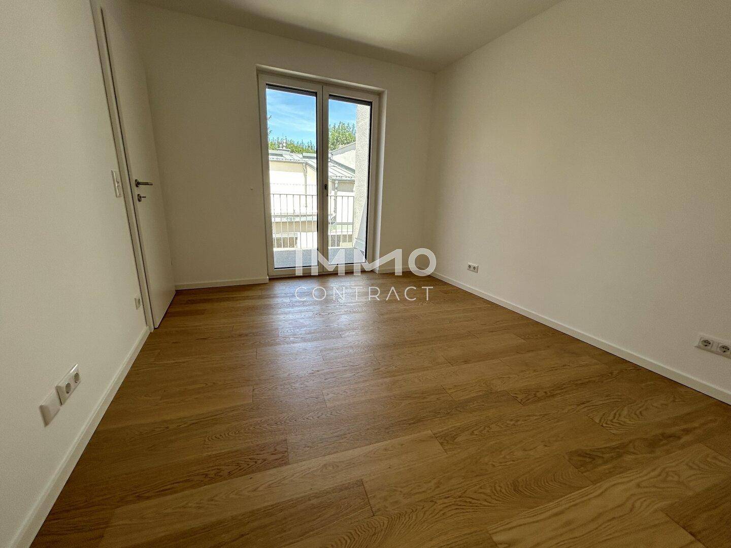 Leeres Zimmer mit Holzboden und Balkonzugang, bietet viel Tageslicht und flexible Gestaltung.
