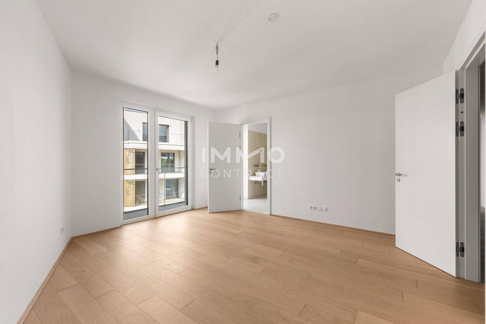 Helles Schlafzimmer mit hellem Holzparkett und Zugang zu einem Balkon.