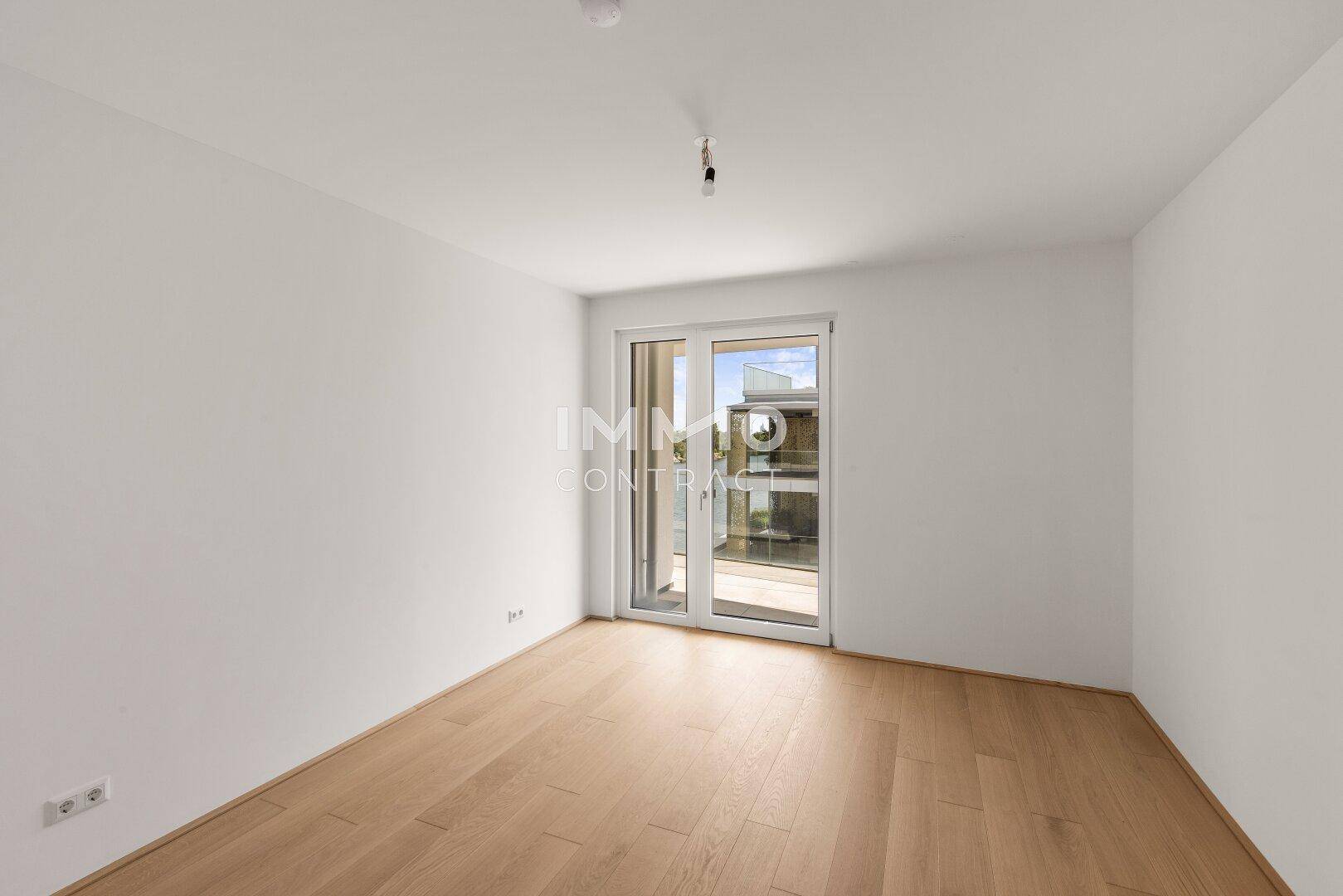 Helles Schlafzimmer mit Parkettboden und Zugang zu einem kleinen Balkon oder einer Loggia.