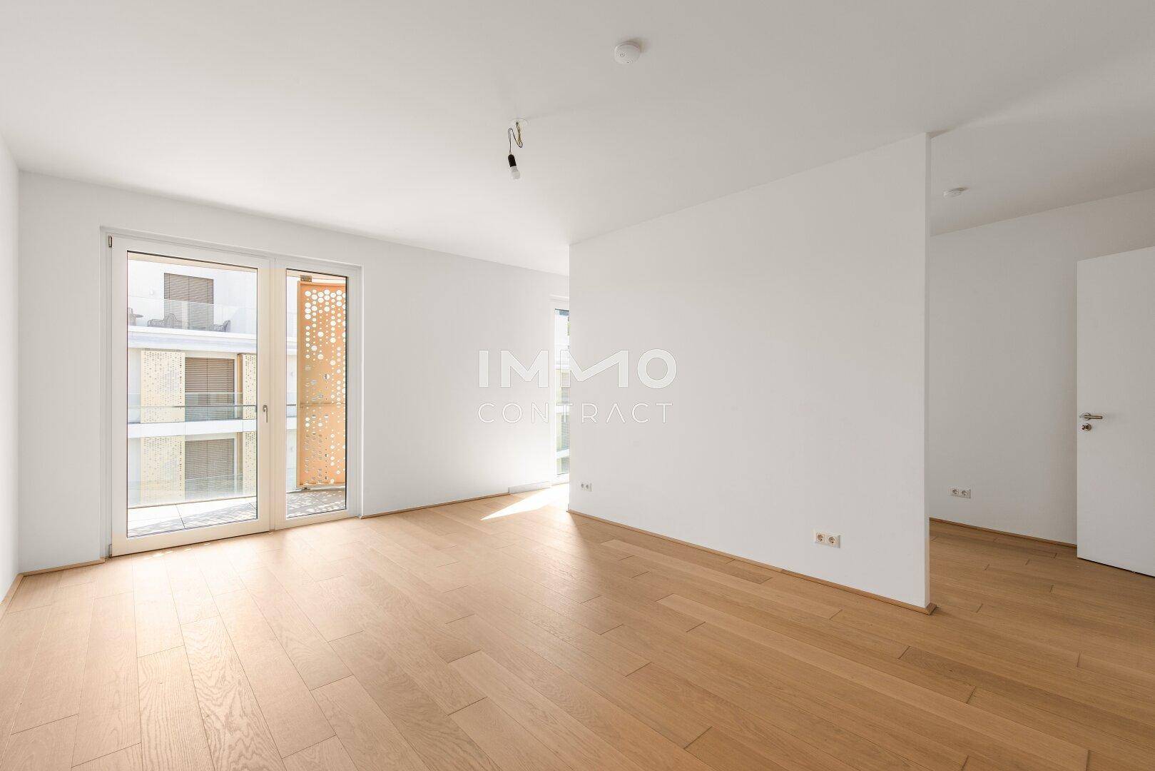 Heller Wohnbereich mit Parkettboden und großen Fenstern, die viel Tageslicht hereinlassen.