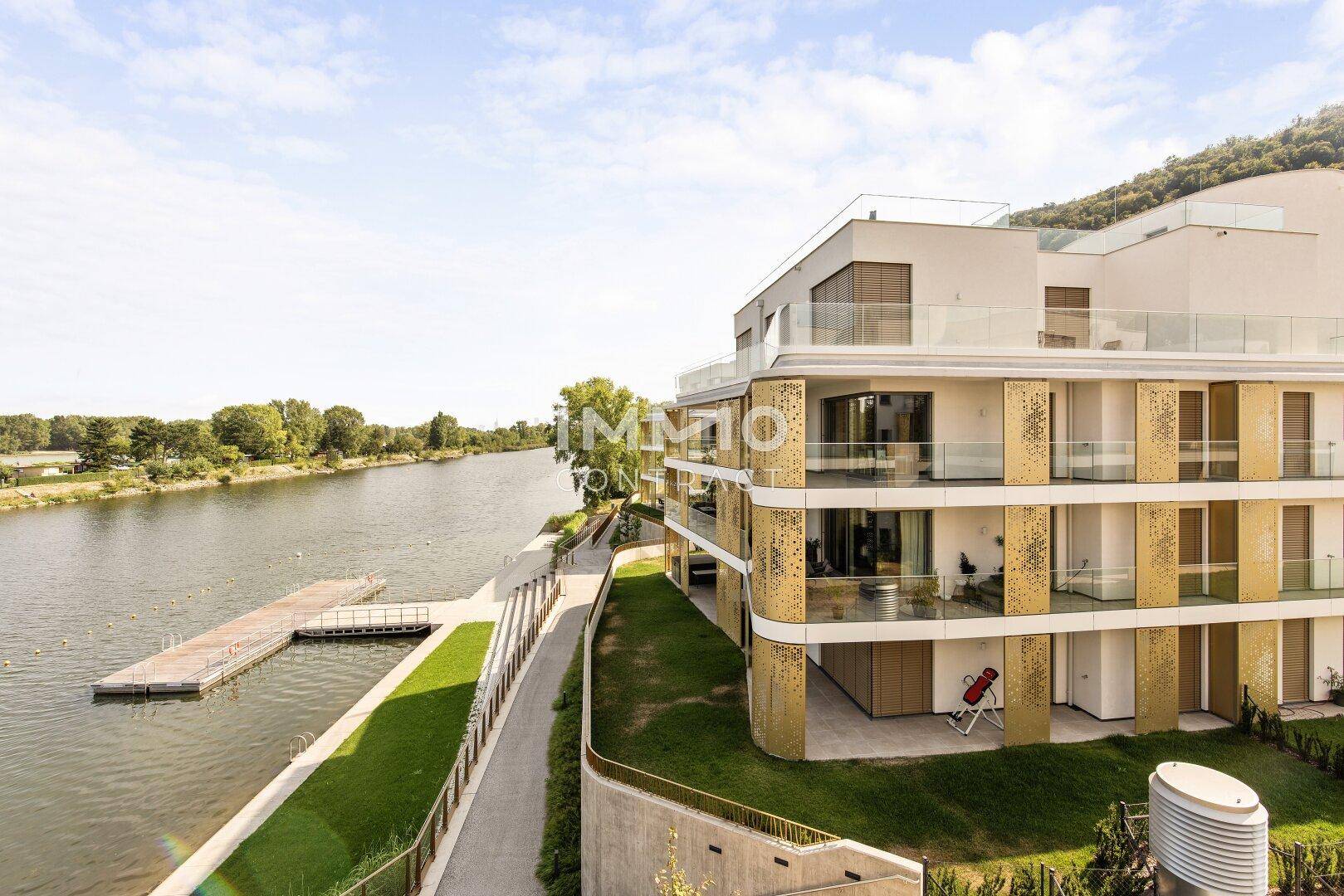 Moderne Wohnanlage am Flussufer mit mehreren Balkonen und Zugang zum Wasser.