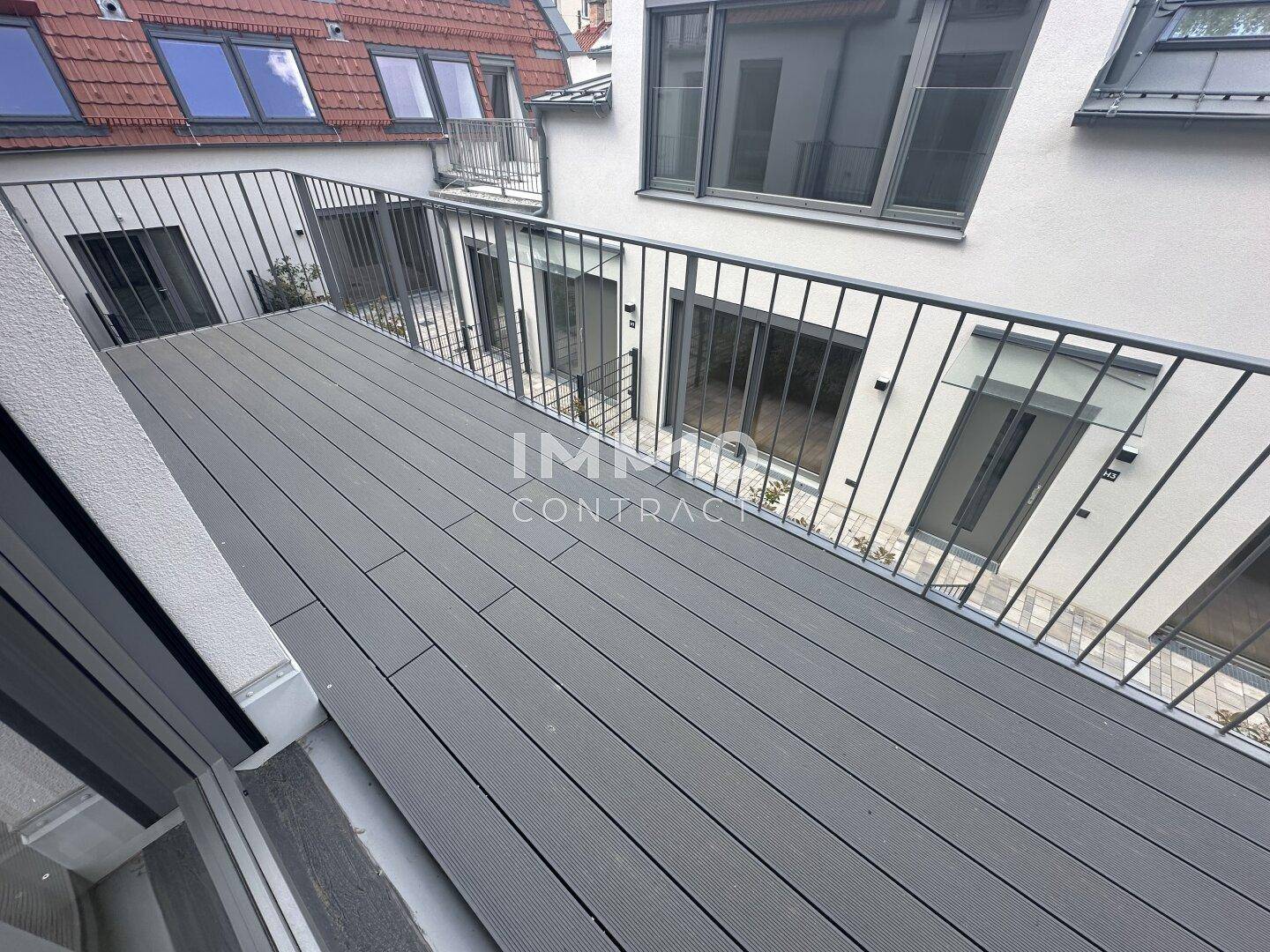 Leerer Balkon mit Holzboden und Blick auf den Innenhof der Wohnanlage, bietet Privatsphäre.