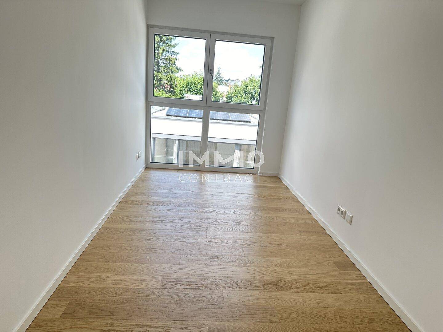 Unmöbliertes Zimmer mit Holzboden und großem Fenster mit Blick auf die Umgebung, vielseitig nutzbar.