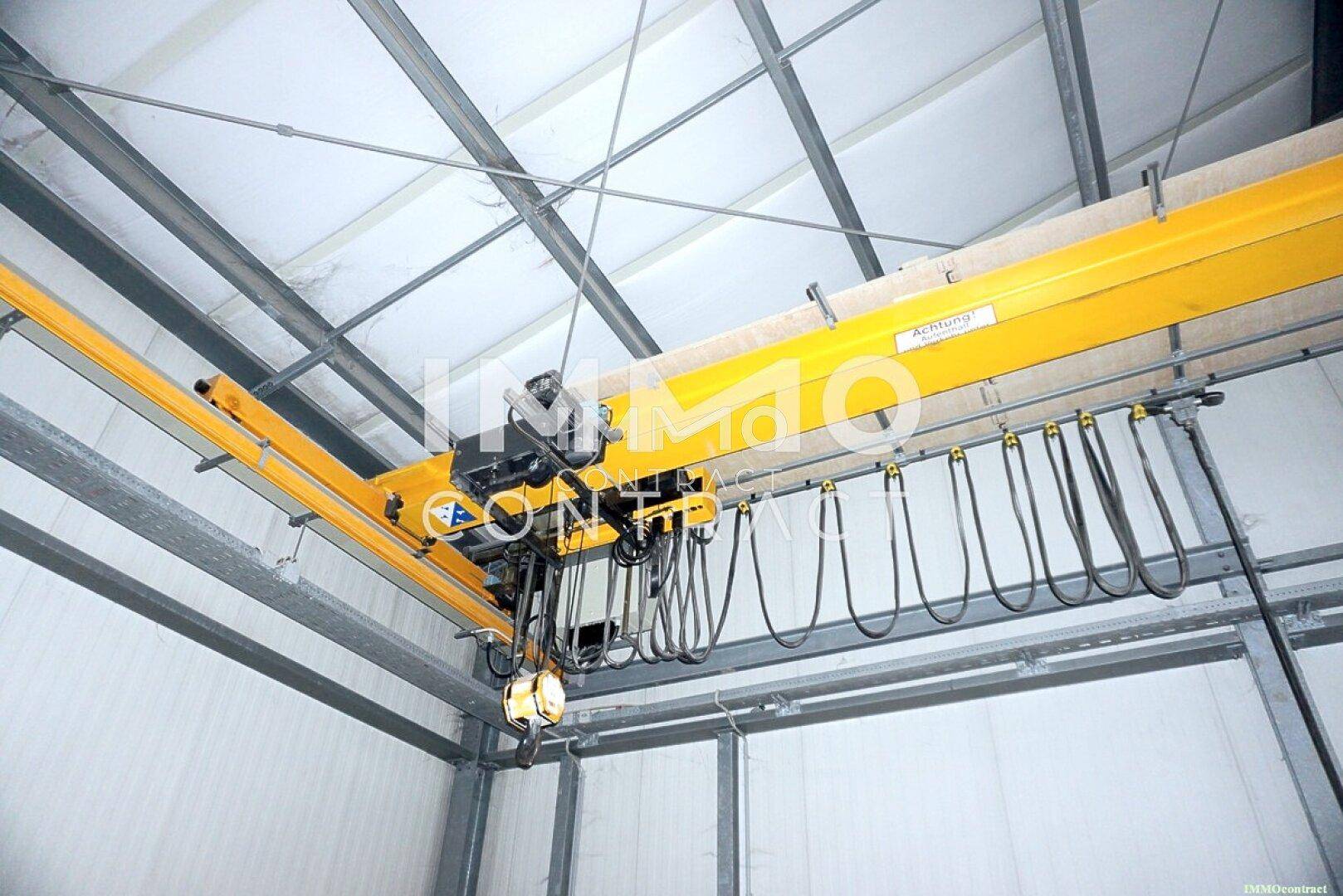 Detailaufnahme eines gelben Laufkrans unter der Decke einer Industriehalle, bereit für schwere Lasten.