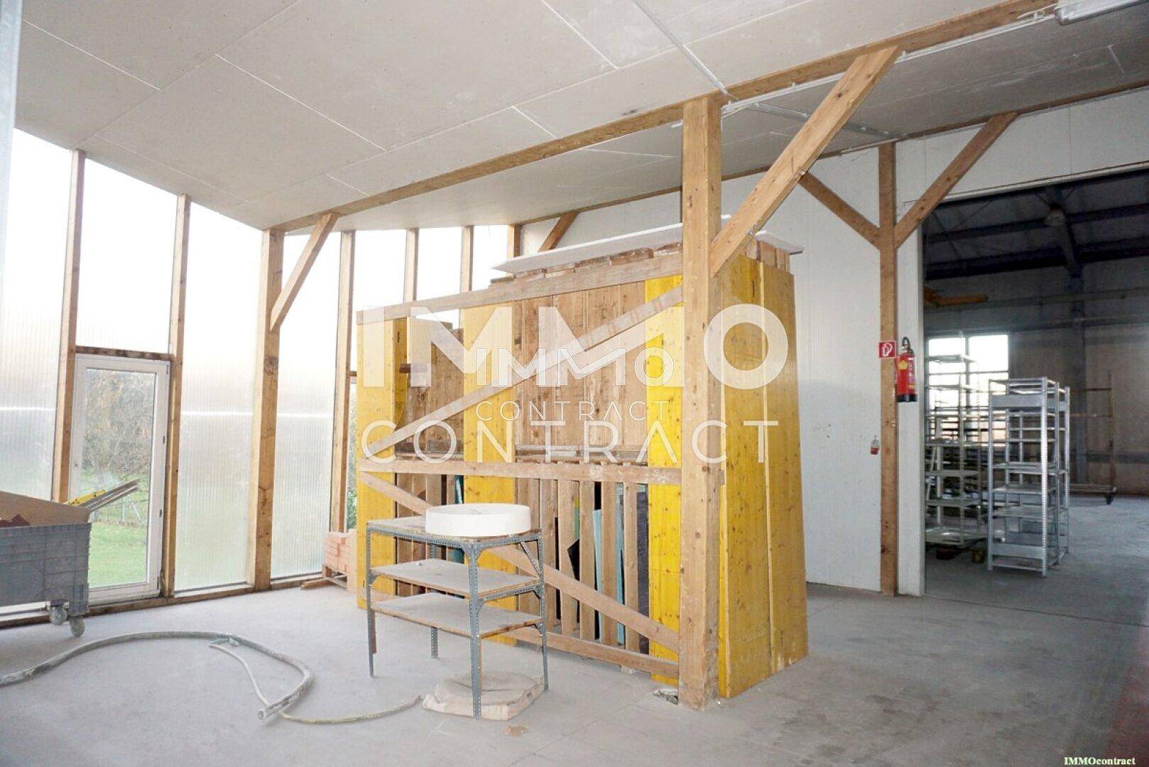 Heller Bereich einer Halle mit Holzbalken, großen Fenstern und Zugang zum Außenbereich.