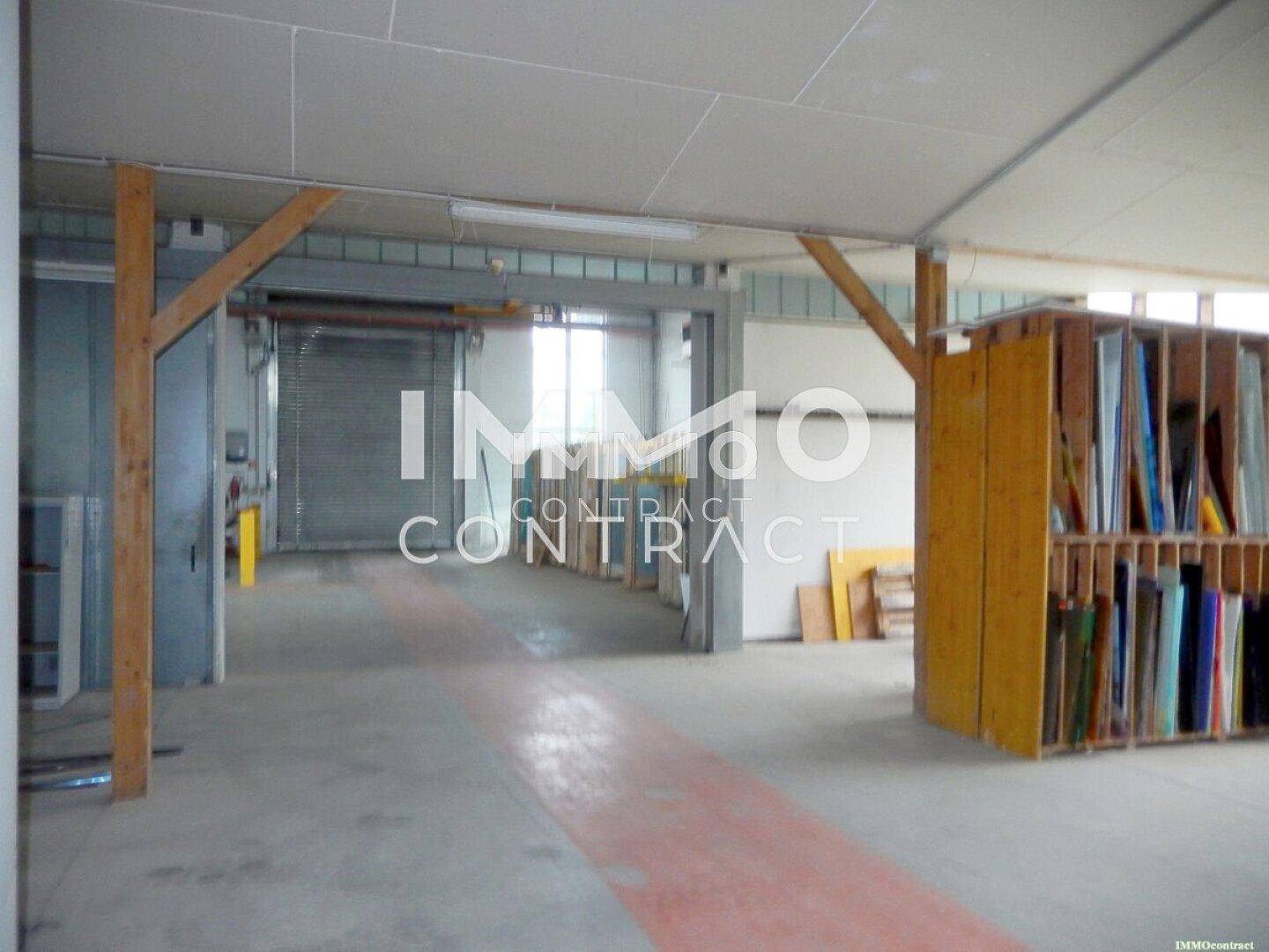 Innenansicht einer Halle mit Holzbalken, Betonboden und Regalen, geeignet für Lagerung oder Werkstatt.