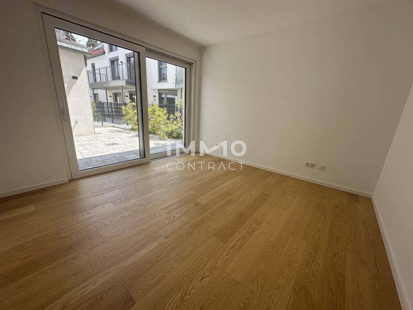 Heller Raum mit Holzboden und großen Fenstern, die einen Blick auf den Innenhof ermöglichen.