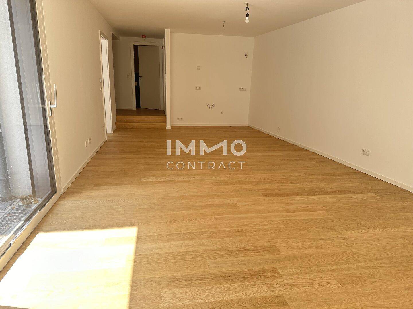 Geräumiges, leeres Wohnzimmer mit hellem Holzboden und viel Tageslicht, bietet Gestaltungsfreiheit.