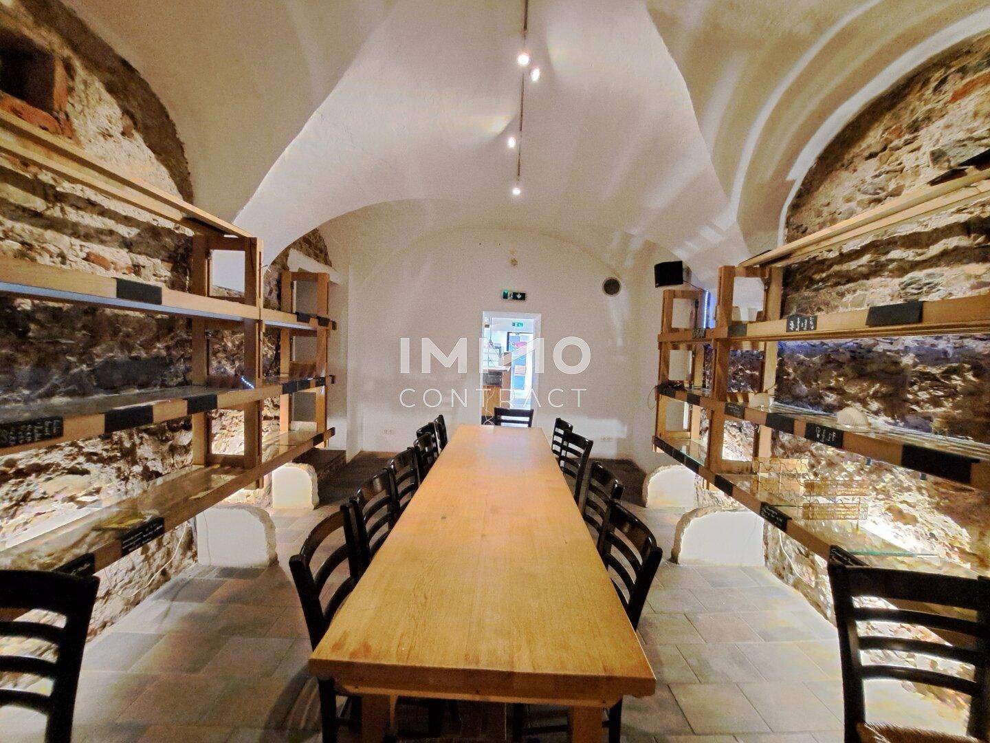 Langer Gewölbekeller mit rustikalen Steinwänden und einer großen Holztafel, perfekt für gesellige Runden.