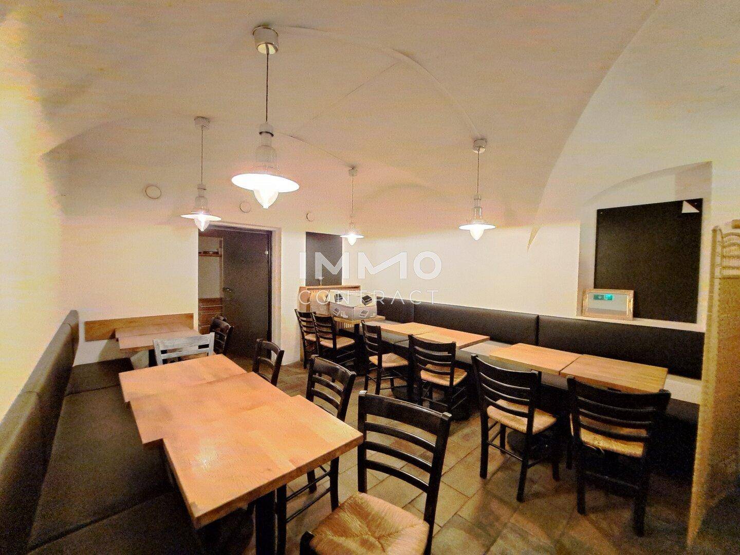 Gemütlicher Gastraum im Gewölbekeller mit Sitzbänken, Holztischen und Pendelleuchten, einladend für Gäste.