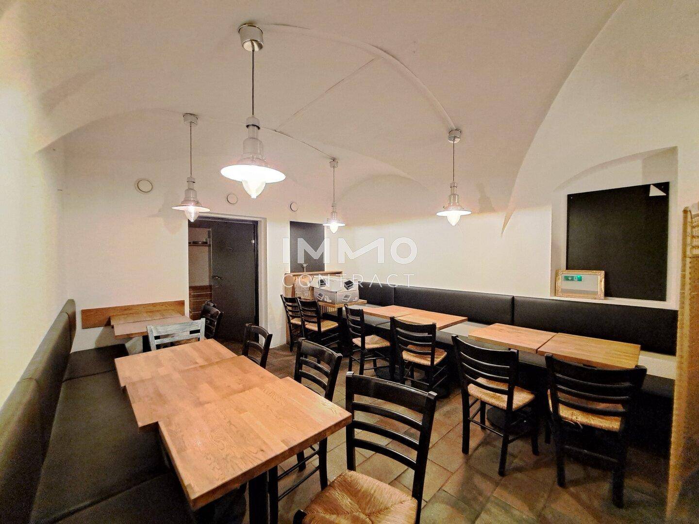 Gastraum im Gewölbekeller mit traditionellen Holztischen und bequemen Sitzbänken, ideal für ein Restaurant.