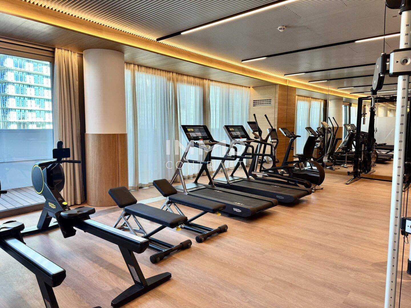 Gut ausgestatteter Fitnessraum mit verschiedenen Trainingsgeräten und Holzboden.