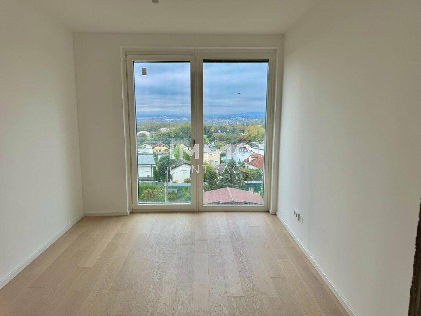 Heller Raum mit Holzboden und großen Fenstern, die einen weiten Ausblick bieten.