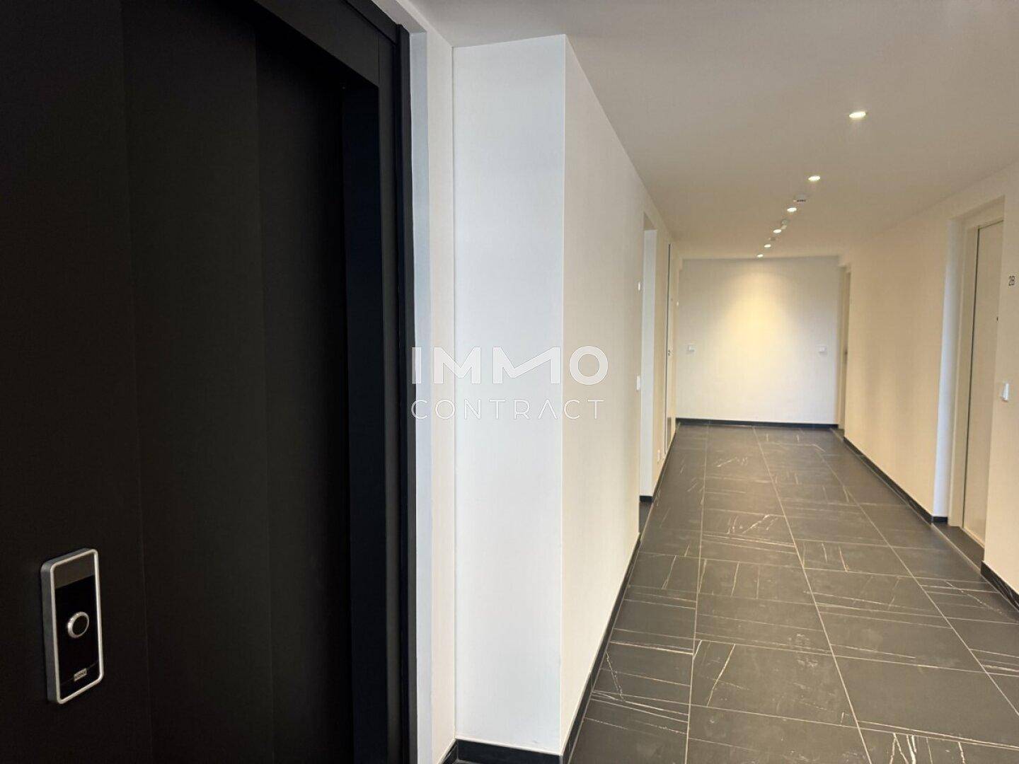 Heller Flur mit dunklen Fliesen und modernem Aufzug in einem Wohngebäude.