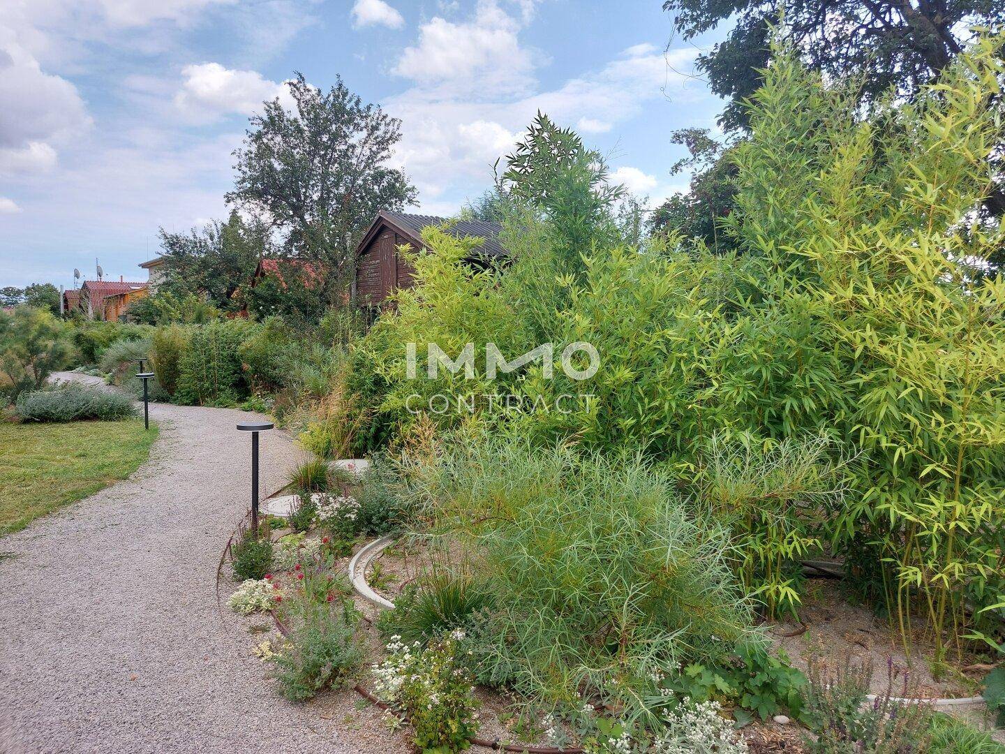 Ein geschwungener Kiesweg führt durch eine üppige Gartenlandschaft mit verschiedenen Pflanzen und Bäumen.