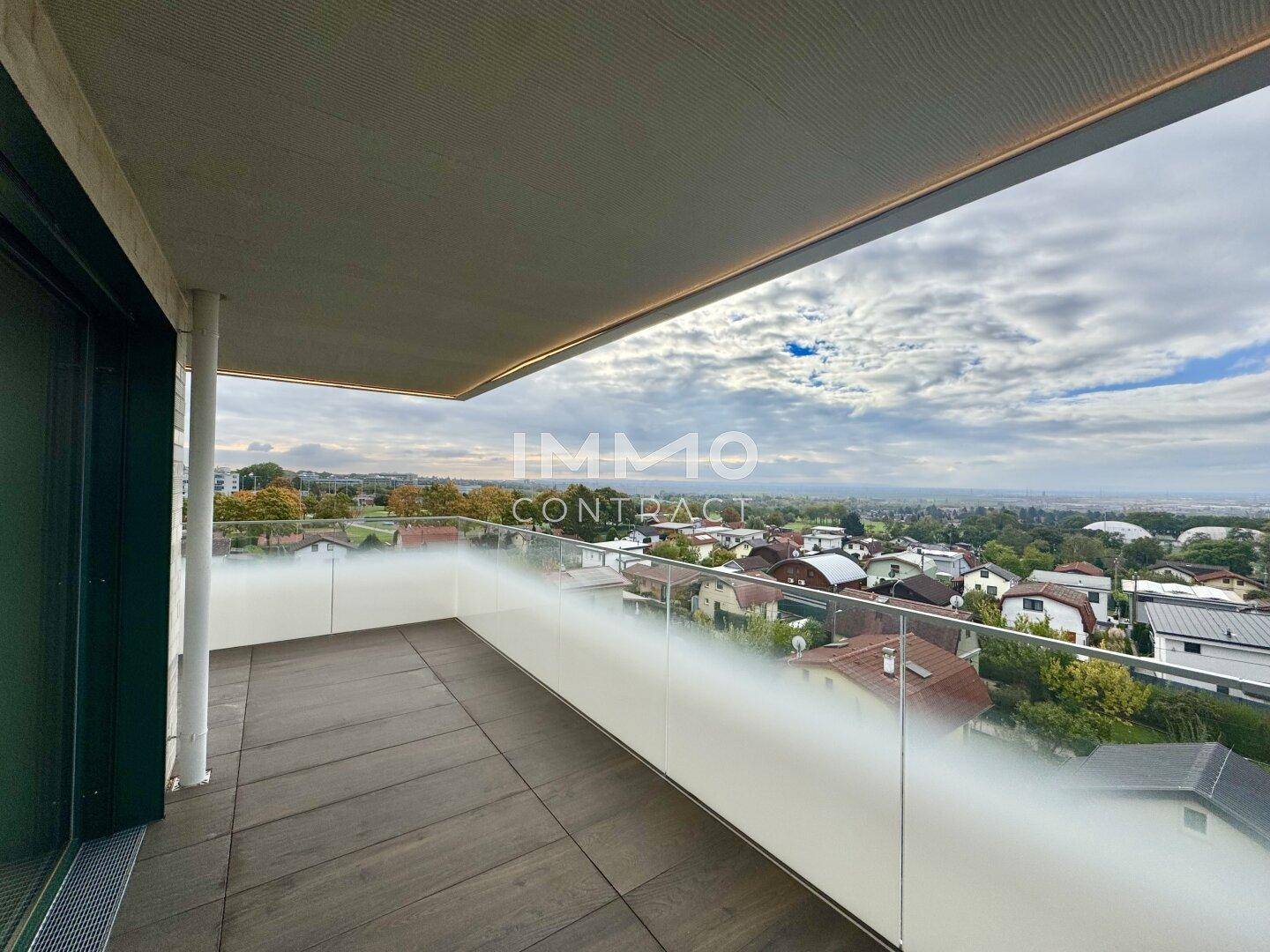 Langer Balkon mit Holzboden und Glasgeländer, ideal für entspannte Stunden im Freien.