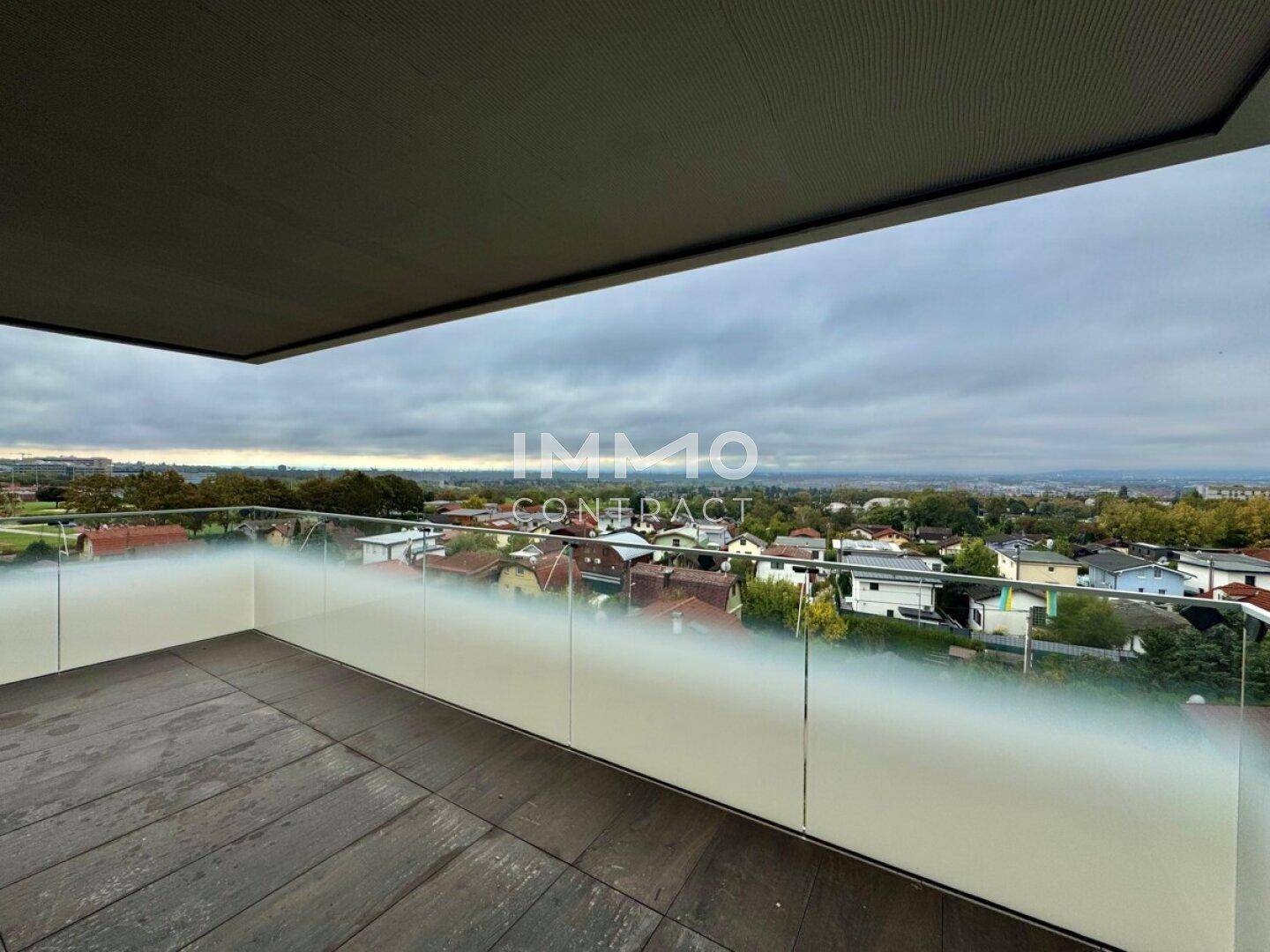 Breiter Balkon mit dunklem Fliesenboden und Glasbrüstung, ideal für entspannte Stunden im Freien.
