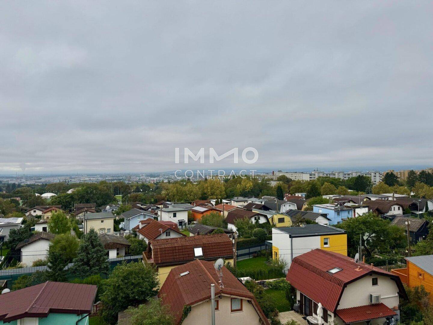 Panoramablick über eine weitläufige Wohngegend mit vielfältigen Dächern und viel Grün.