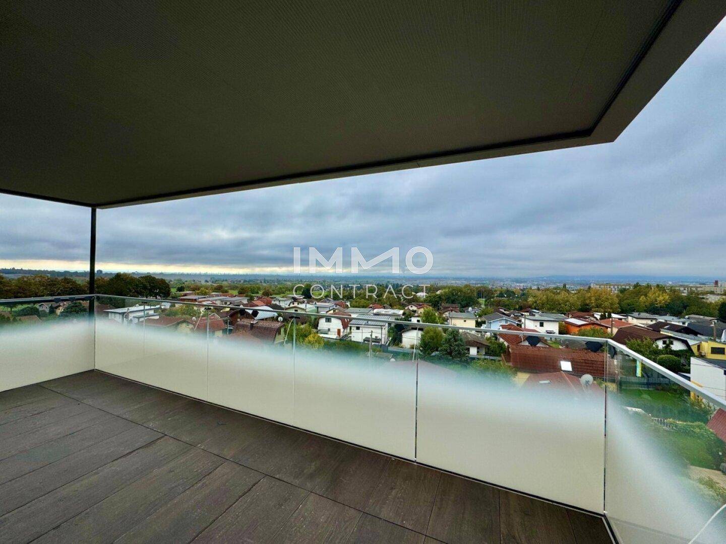 Geräumiger Balkon mit Fliesenboden und Glasgeländer, der einen weiten Blick über die Umgebung bietet.