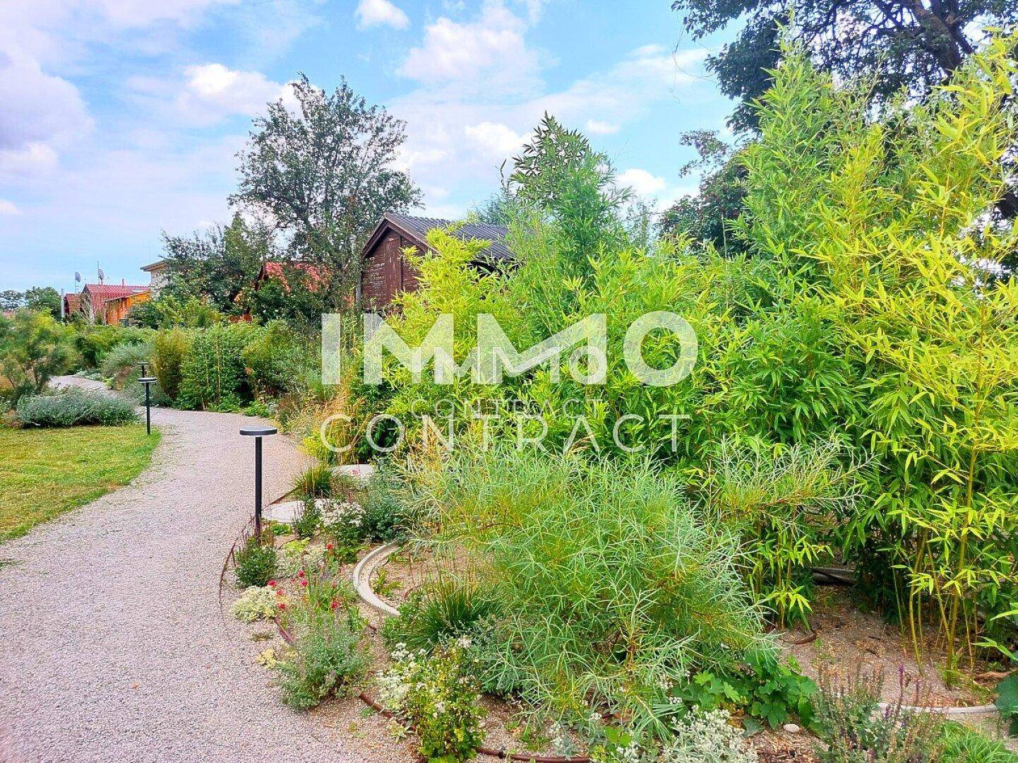 Idyllischer Gartenweg umgeben von üppiger Vegetation und Bäumen, der zu einem versteckten Bereich führt.