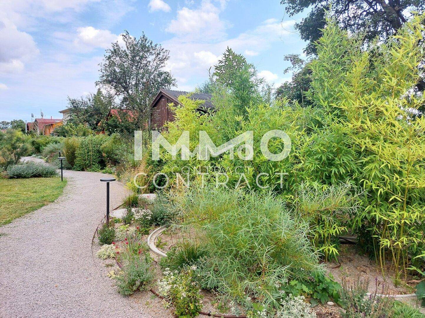 Kiesweg führt durch einen üppigen Garten mit vielfältiger Bepflanzung und hohen Bäumen.
