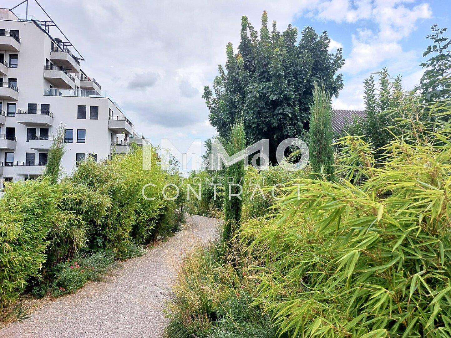 Gepflegter Gartenweg mit üppiger Vegetation und modernen Wohngebäuden im Hintergrund.