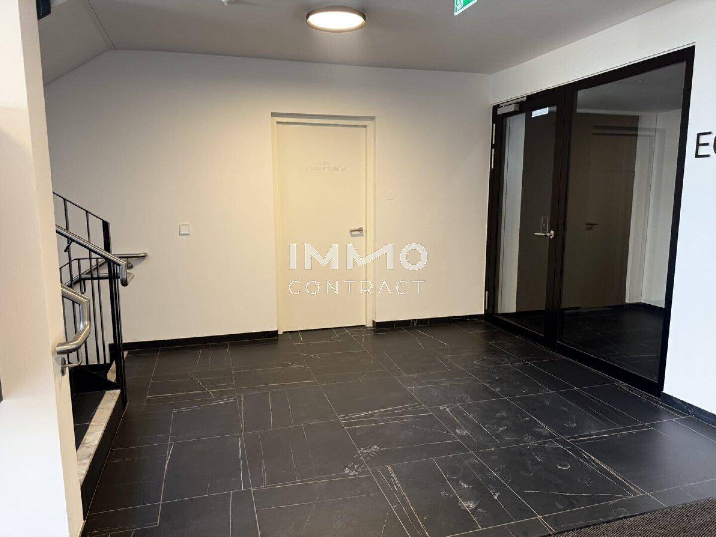 Eingangsbereich mit dunklem Fliesenboden und Treppenaufgang in einem modernen Gebäude.