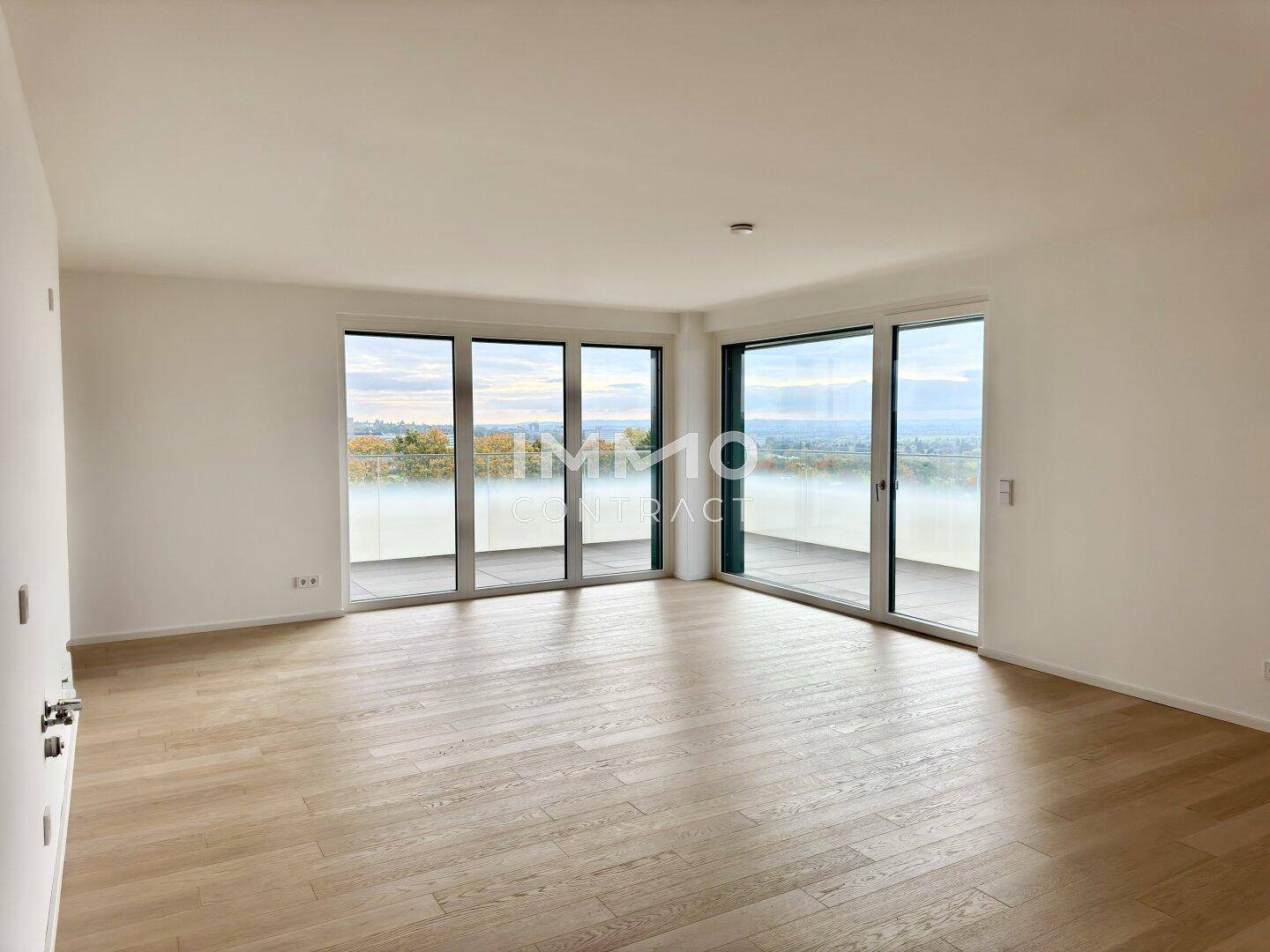 Heller, leerer Wohnbereich mit großen Fenstern und Zugang zum Balkon, bietet weite Ausblicke.