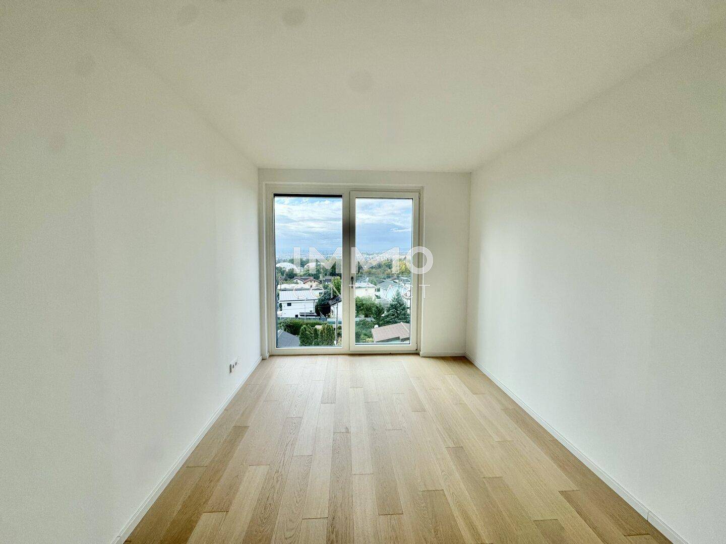Leeres Zimmer mit Parkettboden und Zugang zu einem Balkon, bietet einen weiten Ausblick.