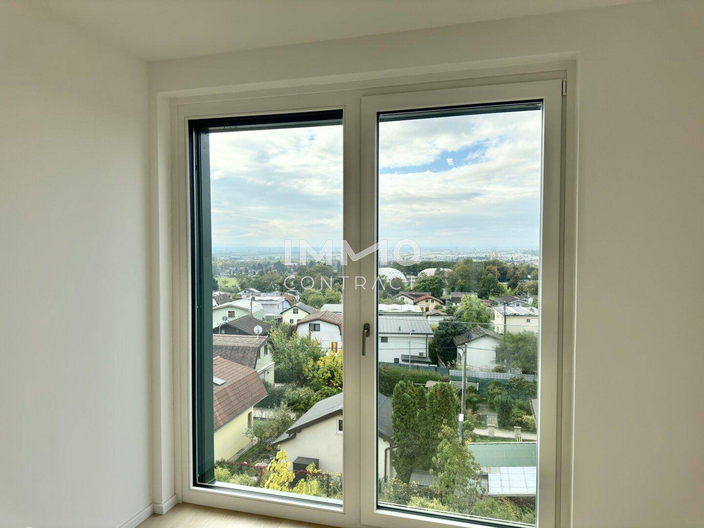Fenster in einem hellen Zimmer mit Blick auf die umliegende Wohngegend und die Landschaft.