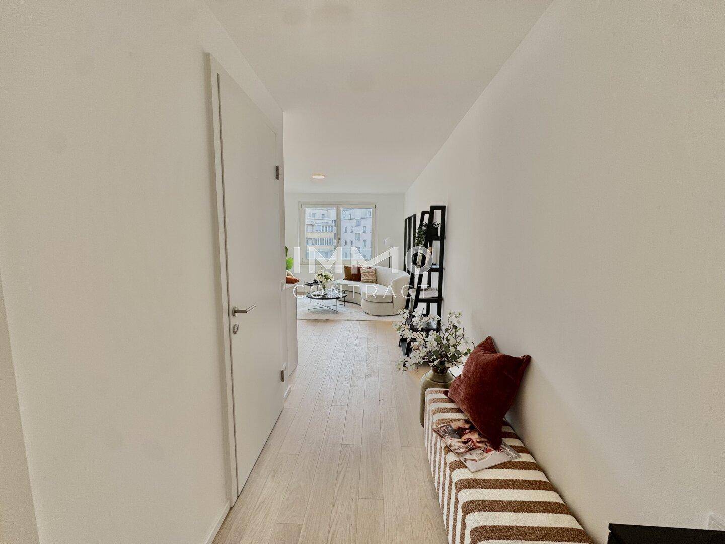 Heller Flur mit Holzboden, weiß gestrichenen Wänden und Blick in den Wohnbereich.