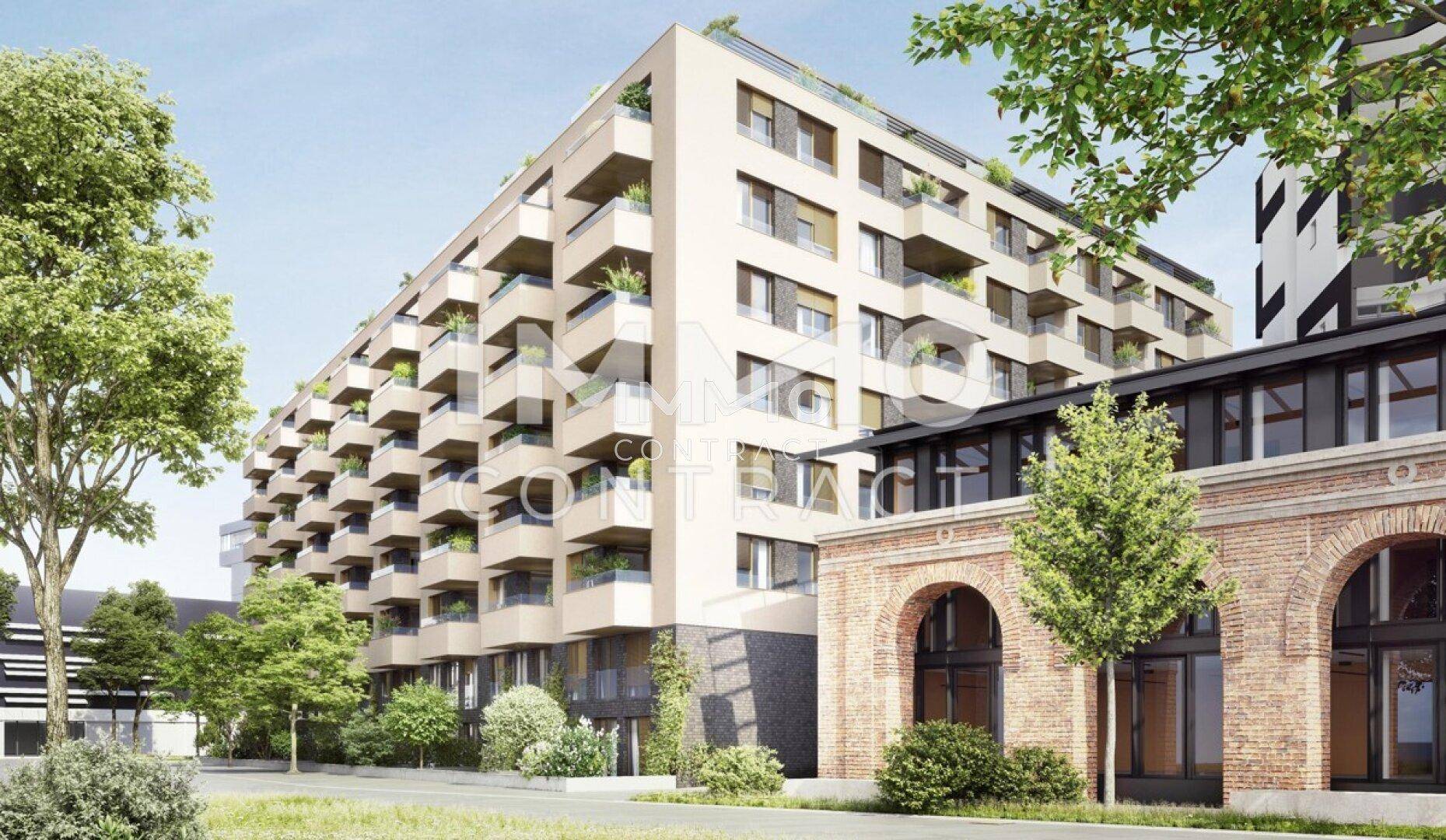 Neubau-Wohngebäude mit vielen Balkonen neben einem historischen Backsteingebäude in grüner Umgebung.