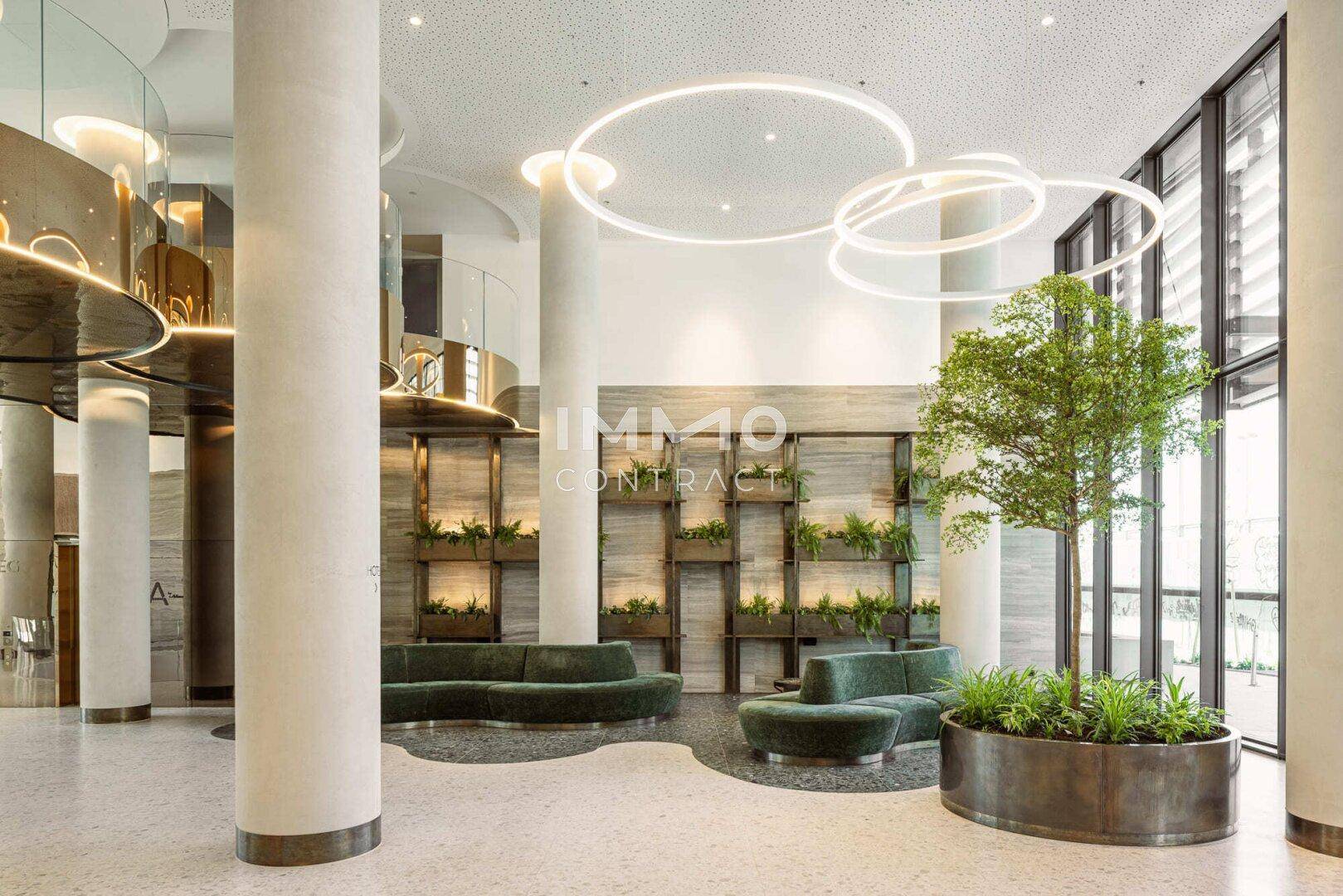 Geräumige Lobby mit bequemen Sitzgelegenheiten, Pflanzen und modernen Deckenleuchten.