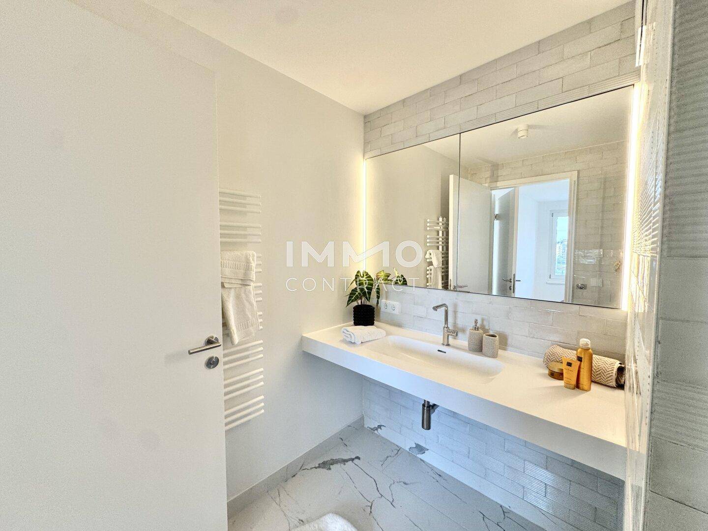 Modernes Badezimmer mit großem Waschbecken, beleuchtetem Spiegelschrank und beheiztem Handtuchhalter.
